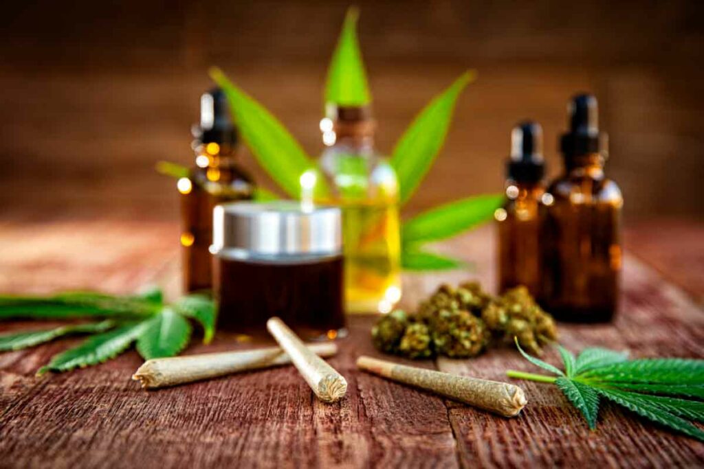 Cannabis leaves, tinctures, and joints on a wood surface