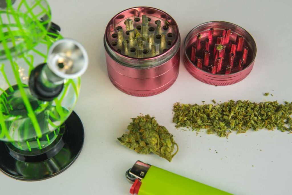 A bong next to a grinder, a lighter, and cannabis flower