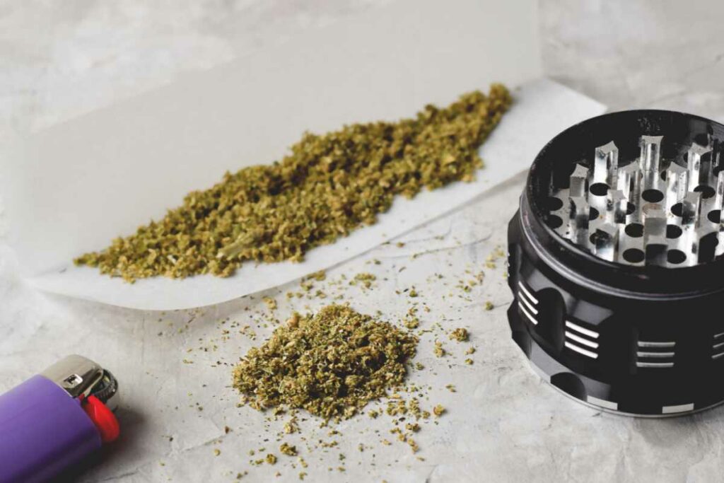 Finely-ground cannabis, rolling paper, a grinder, and a lighter.
